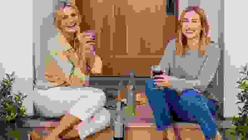 Cameron Diaz and Katherine Power posing on a stoop in front of a wood door and enjoying a glass of Avaline wine.