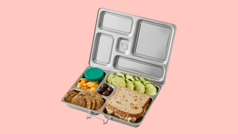 A silver lunch box with a sandwich, snacks, and fruit inside the lunch box.