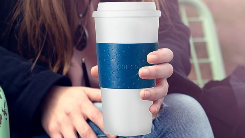 A white woman holds a white cup with a blue band