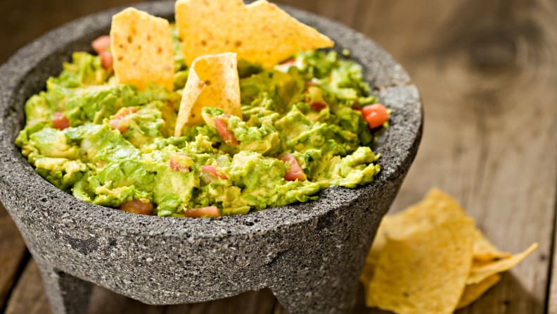 Guacamole cremoso en molcajeta mexicana y primeros planos de chips de maíz crujientes.  Disparo en una vieja mesa de madera al aire libre