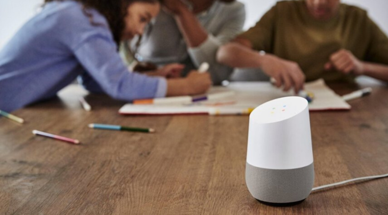 A Google Home speaker is in view with a family playing in the background.