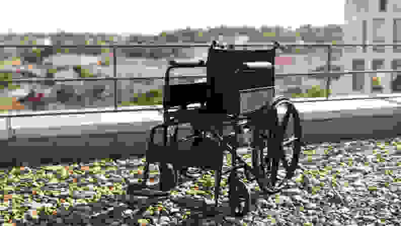 A wheelchair sitting on top of gravel, next to a railing on the top of a building.