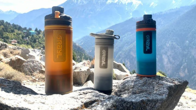 Three Grayl Geopress water bottles appear on a boulder with a mountain scene in the background.