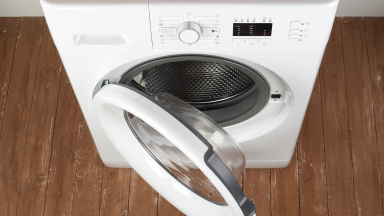 A white ventless dryer sits on a brown floor with its door open