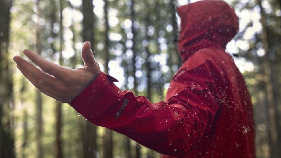 A man wearing a red jacket with Gore-Tex technology embedded into it, holding his hand out to feel the rain.