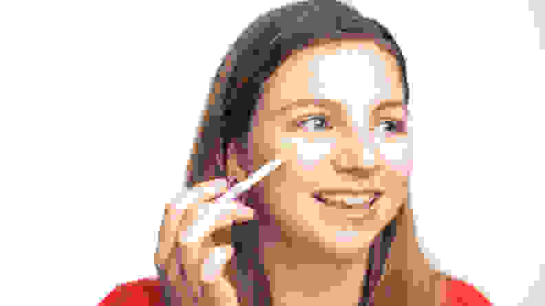 A woman applying concealer to her face.