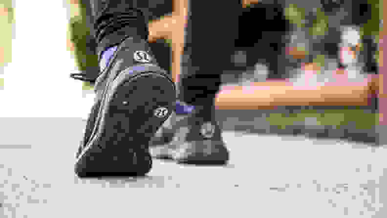 Feet wearing black Lululemon shoes with the brand's logo in white on the heel