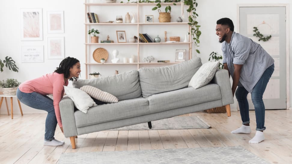 A smiling couple moves a sofa into a living room together.