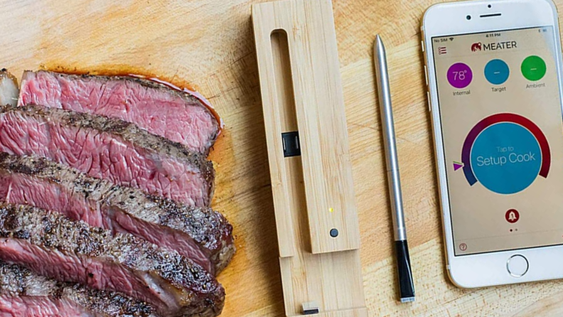 A slab of meat and meat thermometer sit on a butcher block.