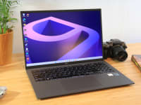 A laptop sits on a desk surrounded by a house plant, video game device, camera, and book.