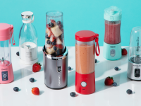 Six portable blenders sit on a white surface surrounded by berries.