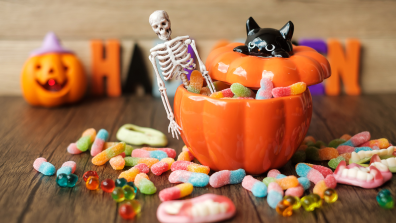 Assorted Halloween candy inside of glass candy jar amongst festive decor items.