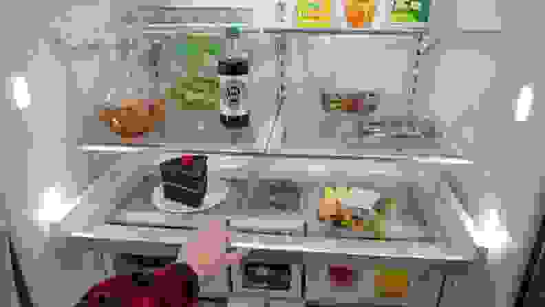 A close-up of the Whirlpool fridge's interior, with a hand reaching in to pull out its platter tray. The shelves and bins are all stocked with food.