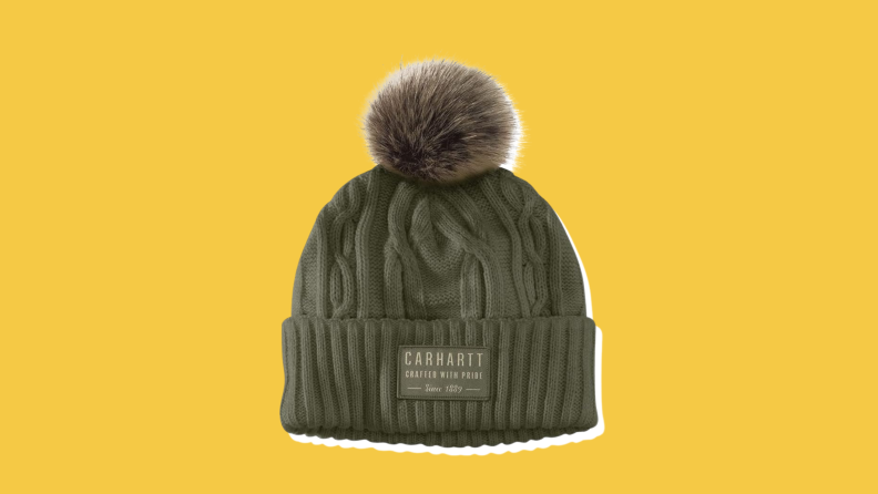 A dark green Carhartt Pom Beanie on a yellow background.