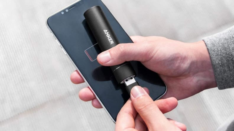 A person charges their smartphone using an Anker portable battery pack.