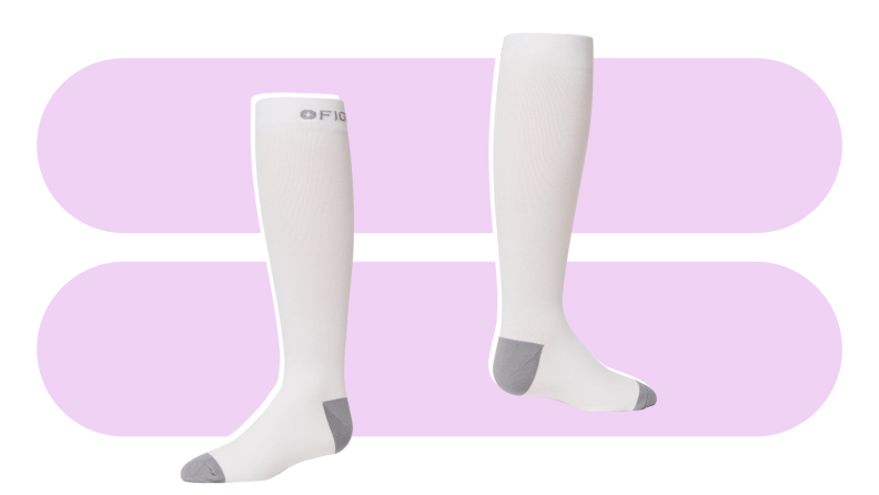 Two tall, white Fige compression socks on a light purple background.