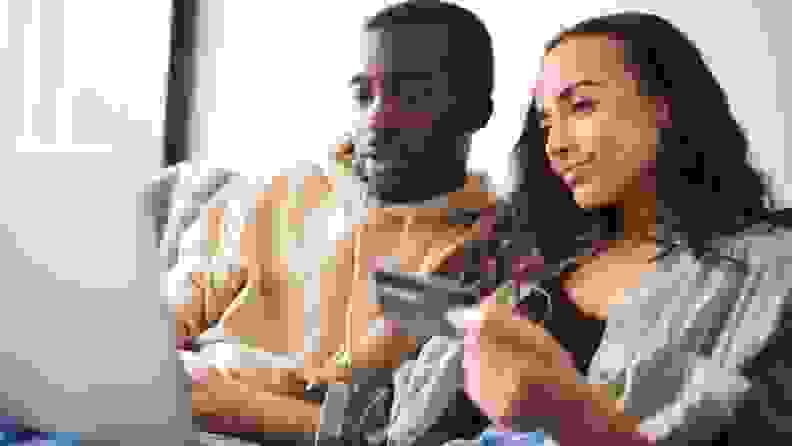 A couple sits on a couch as they look at a computer screen and hold up a credit card