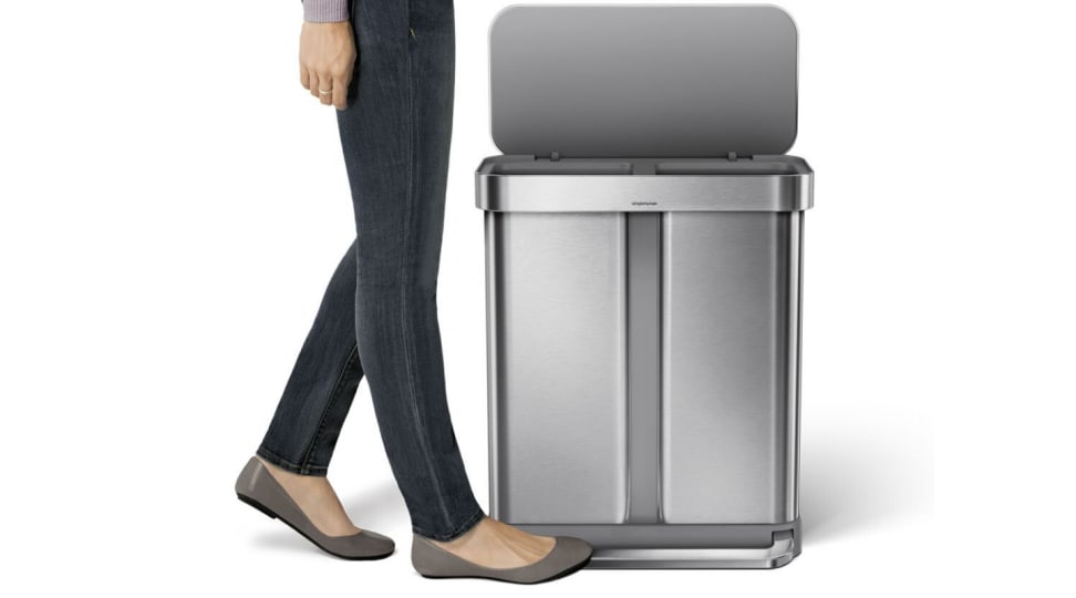 A woman's foot steps on the pedal bar to open the Simplehuman dual compartment trash can.