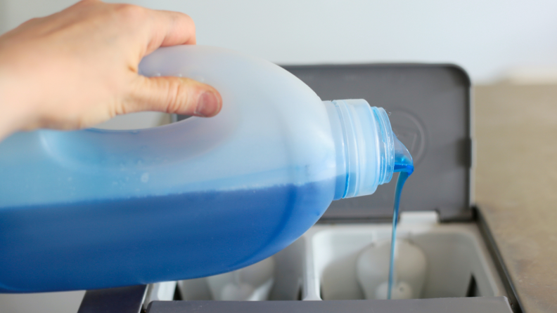 Blue detergent being poured into detergent dispenser of washing machine.