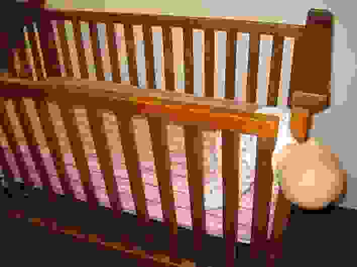A drop sided crib with a doll caught in the opening to demonstrate potential dangers and injuries.
