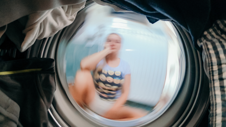A person peers into the blurry window of a spinning washing machine.