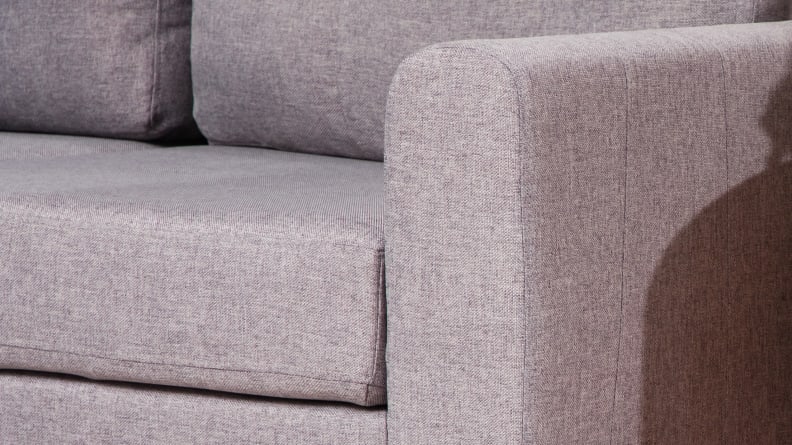 A close-up of the gray upholstered cushion and fabric of the couch's armrest.