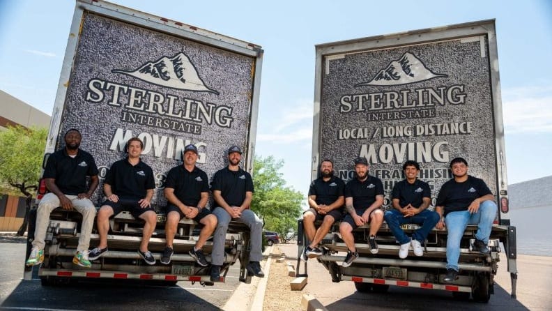 Two moving trucks with four movers seated at the back of each truck