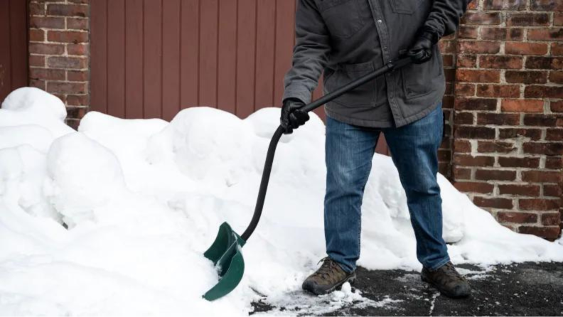 A person shoveling snow against a brick building.