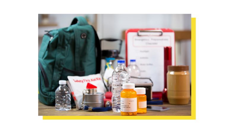 Emergency preparedness bag next to medication, bottles of water, jar of peanut butter, and first aid kit and clip board.