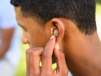 A person pushes a hearing aid into their ear in an outside setting
