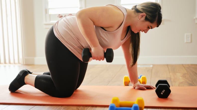 A woman using dumbbells on a yoga mat.