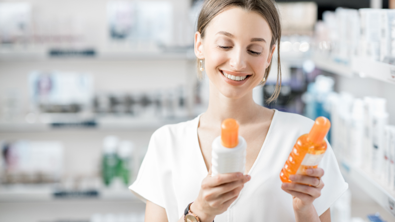 A woman in the beauty aisle smiling while holding two beauty products