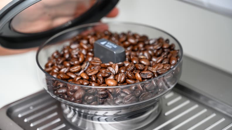 A close-up of the Barista Touch's built-in burr grinder filled with coffee beans.