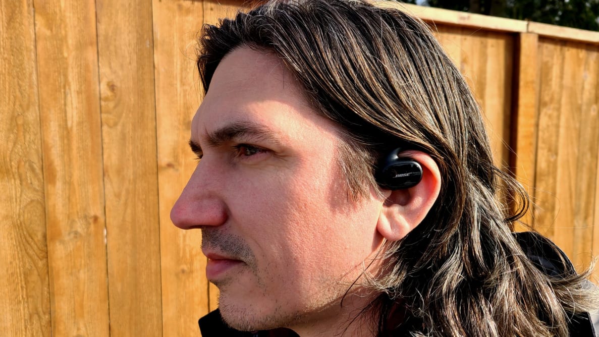 Bose Sport Earbuds listening with earbuds in left ear in front of cedar planks