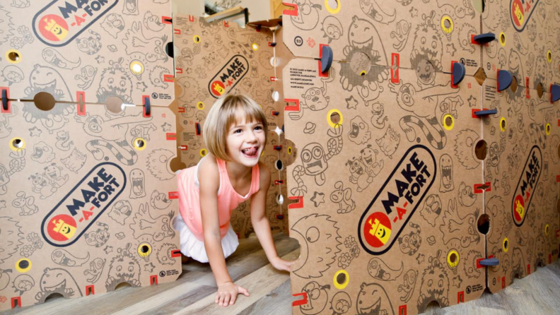 A child laughs inside her cardboard play fort