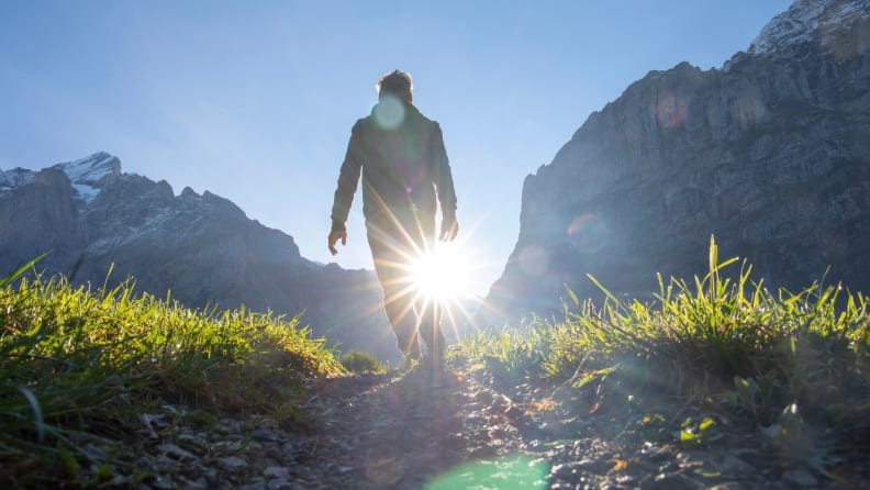 A man walking down a trail with the sun illuminating him from behind