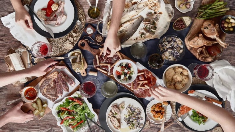 Campo Grande variety of meats, veggies, and dips spread out on a table with people reaching to grab different foods.