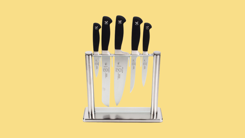 Five knives of various sizes stored in a glass block against yellow bacgkround