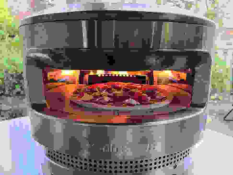 The Solo Pi sits on a counter outside. There's fire in the back of the oven and a pizza inside.
