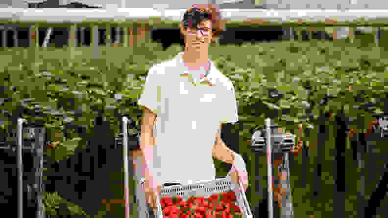 Smiling teenager with Cerebral Palsy holding a plastic bin of strawberries in a field outdoors.