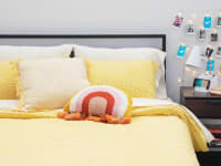 A dorm room with a yellow comforter on a bed, string lights, and polaroid photos on display.