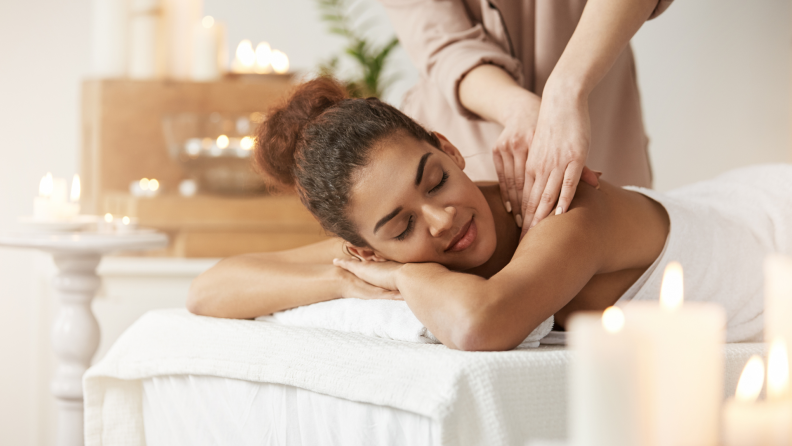 A woman enjoys a relaxing massage in a candlelit spa setting with a serene ambiance.