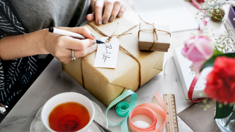 Person tying ribbon on paper-wrapped present.