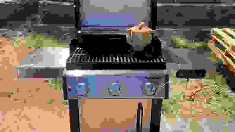 A Weber smart grill with the top open and a whole chicken cooking.