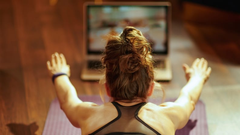 A woman exercising in front of her laptop on a yoga mat.