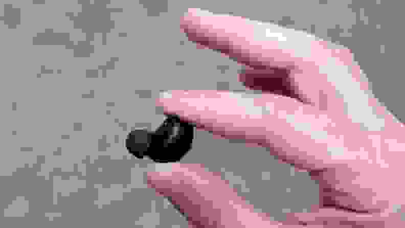 A hand is holding the all black Raycon earbud to show its diminutive size.