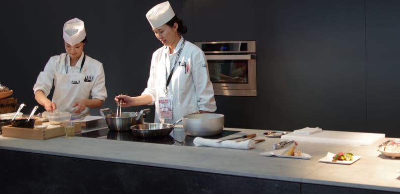 Chefs prepare traditional Japanese food using a Panasonic wall oven and induction cooktop.
