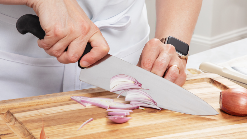 Hand using a chef's knife to slice a shallot on a cutting board