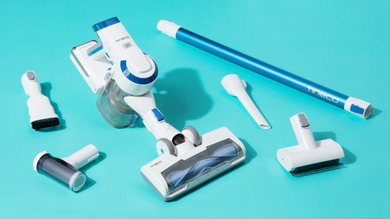 A white cordless stick vacuum is unassembled in 6 parts on a blue background