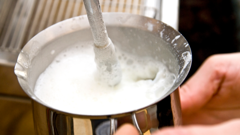 A person steams hot milk for an espresso with a steam wand.